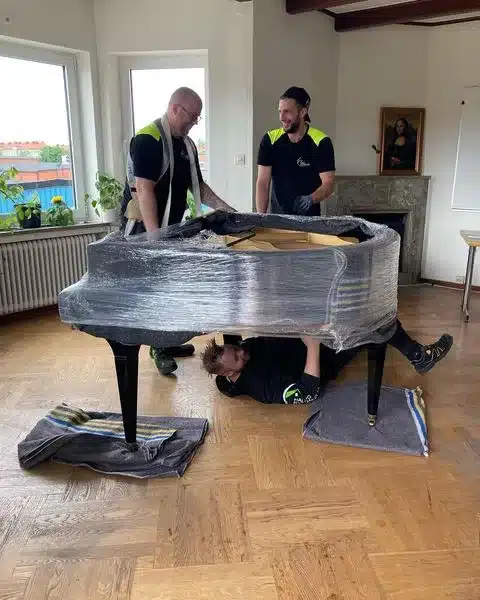 Tre personer emballerar en flygel i en lägenhet