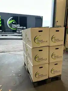 Sex staplade flyttkartonger märkta Malmö Flyttjänst AB bredvid en öppen lastkaj.